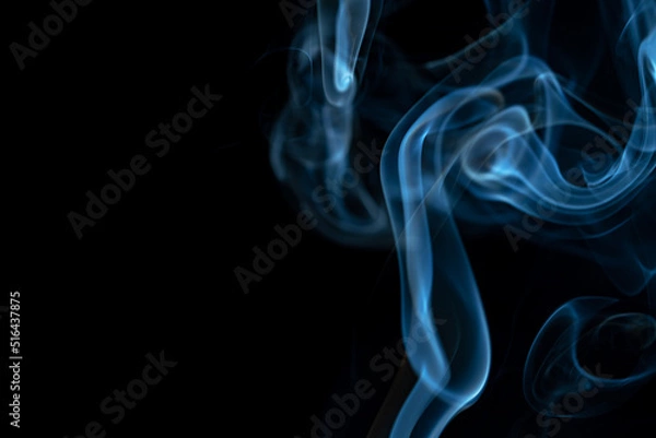 Fototapeta White blue cloud of smoke from smoking a cigar on an isolated black background. Fumes from smolder cigarette floating in the space. Smoke flying in the air and illuminated by light. Macro shot.