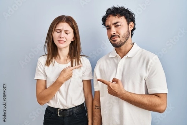 Fototapeta Young couple wearing casual clothes standing together pointing aside worried and nervous with forefinger, concerned and surprised expression