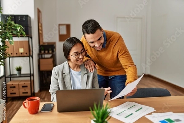 Fototapeta Two business workers smiling happy working sitting on desk at the office.