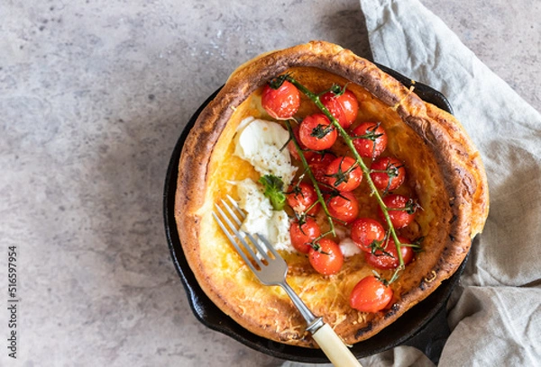 Obraz Savory Dutch baby pancake with roasted cherry tomatoes, mozzarella cheese and green salad leaves in serving cast-iron frying pan. Danish cuisine. Hearty breakfast.