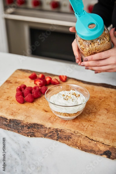 Obraz A woman topping yogurt with granola in a bright modern kitchen