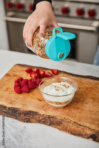 Obraz A woman topping yogurt with granola in a bright modern kitchen