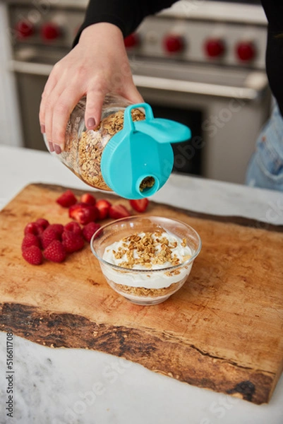 Obraz A woman topping yogurt with granola in a bright modern kitchen