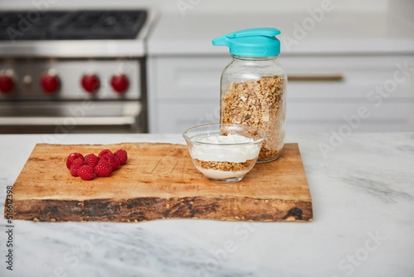 Obraz Yogurt with granola, and raspberries and strawberries next to jar with granola in a bright modern kitchen