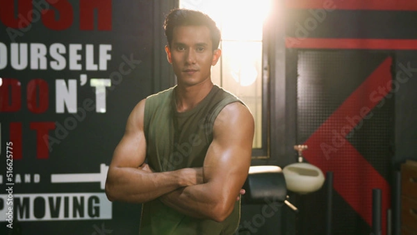 Obraz Close-up or closeup shot of Asian athlete man crossing one's arm pose with confident face in fitness gym. Muscular male bodybuilder looking at camera with positive emotion. Bodybuilding at gym concept
