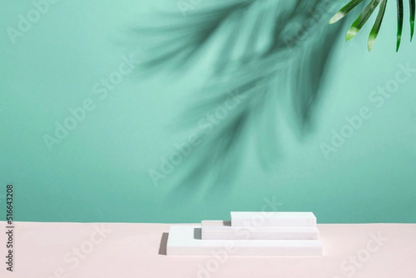 Fototapeta Abstract podium pedestal from white marble, blue menthol empty background deep shadows from plant