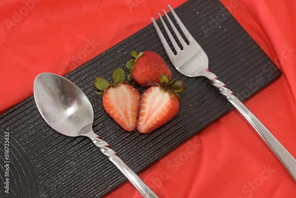 Obraz vivid red strawberry on black ceramic dish on red background with silverware