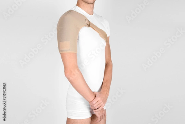 Fototapeta Shoulder joint orthosis or brace isolated on white background. A man in a support orthopedic bandage on his arms after surgery, suffering from shoulder pain, the result of a work injury.