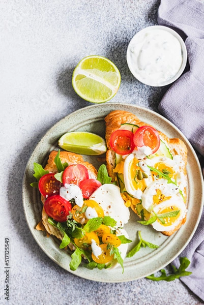 Obraz Variety of croissant sandwiches with tomato, cucumber, mozzarella cheese, eggs and mashed avocado with mint and arugula. Open savory sandwiches. Tasty healthy breakfast.