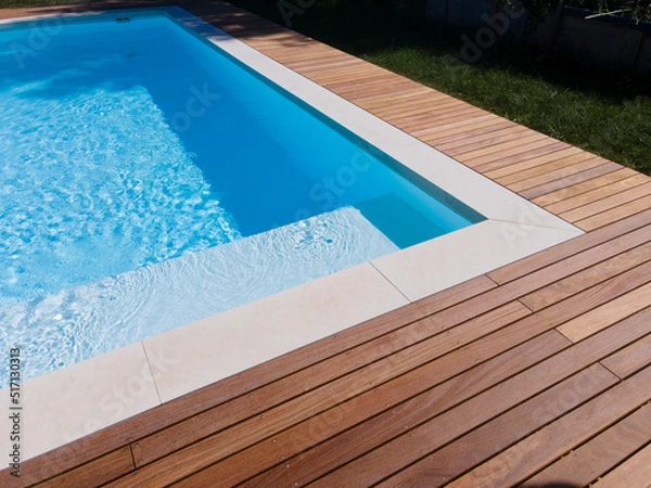 Fototapeta Drone flight over pool with nice wooden terrace surrounded by green lawn in beautiful garden