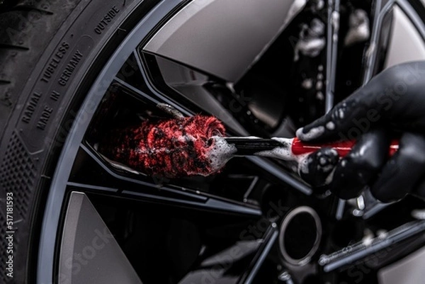 Obraz Employee of a car wash or a car detailing studio carefully washes a car rim with a special brush