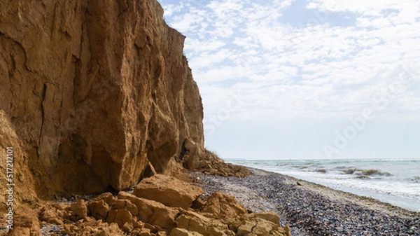 Obraz Ruined clay slope by the sea. Cracked clay cliff on the coast. A crumbling and cracked clay wall on the beach.