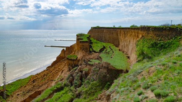 Obraz Ruined clay slope by the sea. Cracked clay cliff on the coast. A crumbling and cracked clay wall on the beach.
