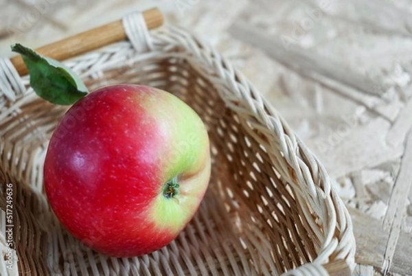 Fototapeta Red apple in a wicker basket on a wooden background, copy space