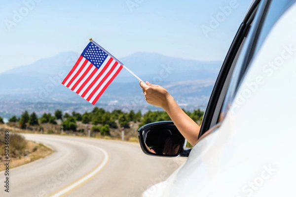 Fototapeta Woman holding USA flag from the open car window driving along the serpentine road in the mountains. Concept