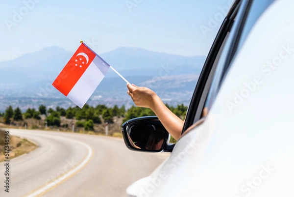 Fototapeta Woman holding Singapore flag from the open car window driving along the serpentine road in the mountains. Concept