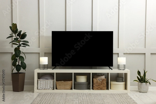 Fototapeta Modern TV on cabinet and beautiful houseplants near white wall in room. Interior design