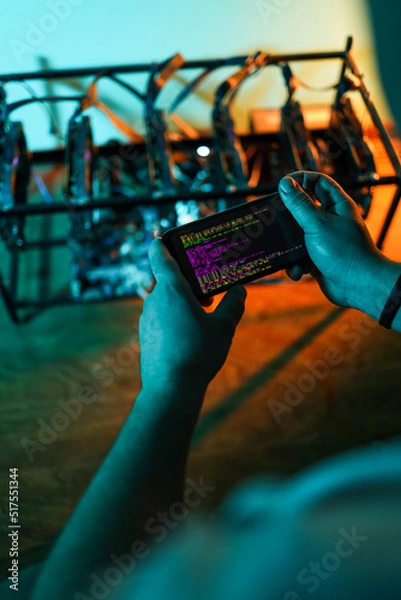 Fototapeta Male programmer adjusting cryptocurrency mining rig to optimal settings with mobile phone