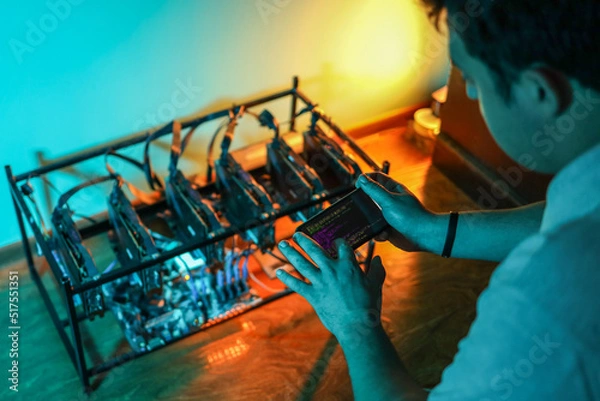 Fototapeta Male programmer adjusting cryptocurrency mining rig to optimal settings with mobile phone