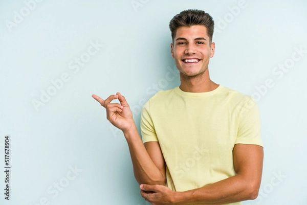 Fototapeta Young caucasian man isolated on blue background smiling cheerfully pointing with forefinger away.