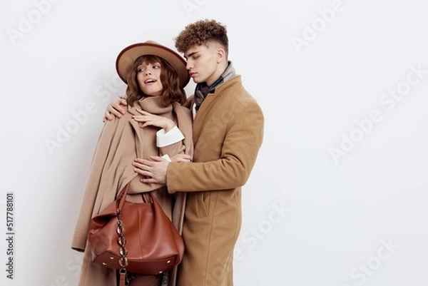 Fototapeta a cute couple in love a man and a woman in a stylish autumn rain stand hugging on a white background and a woman holds a brown bag in her hand