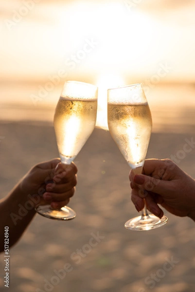 Obraz Champagne glasses cheers on the beach at sunset with sun behind