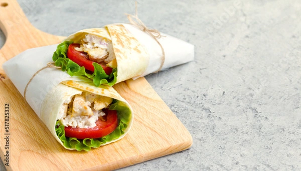 Fototapeta shawarma with chicken, tomatoes, sauce and lettuce on a wooden board. gray background with a place for an inscription
