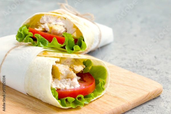 Fototapeta shawarma with chicken, tomatoes, sauce and lettuce on a wooden board. close-up