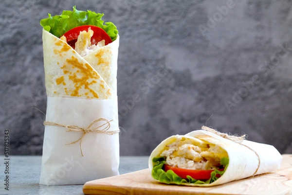 Fototapeta shawarma with chicken, tomatoes, sauce and lettuce on a wooden board. gray background with a place for an inscription
