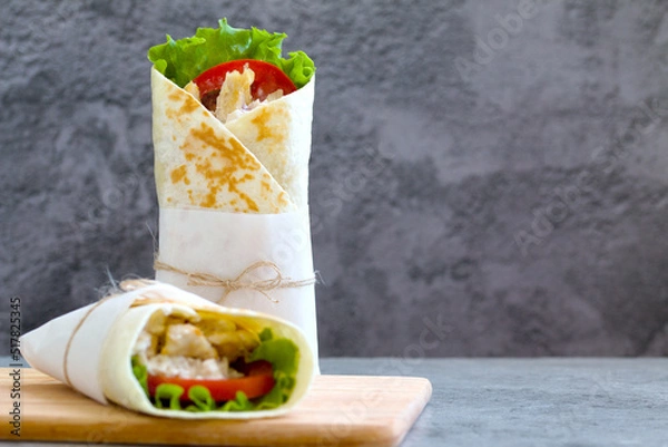 Fototapeta shawarma with chicken, tomatoes, sauce and lettuce on a wooden board. gray background with a place for an inscription