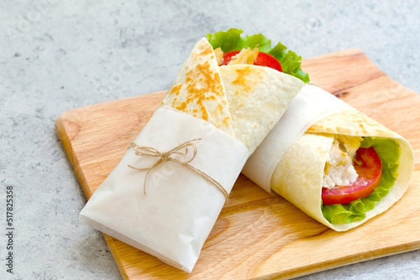 Fototapeta shawarma with chicken, tomatoes, sauce and lettuce on a wooden board. close-up