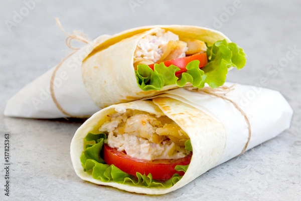 Fototapeta shawarma with chicken, tomatoes, sauce and lettuce on a gray background. close-up