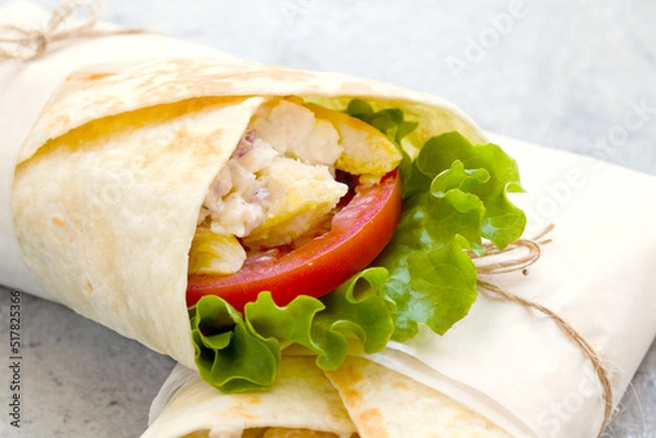 Fototapeta shawarma with chicken, tomatoes, sauce and lettuce on a gray background. close-up