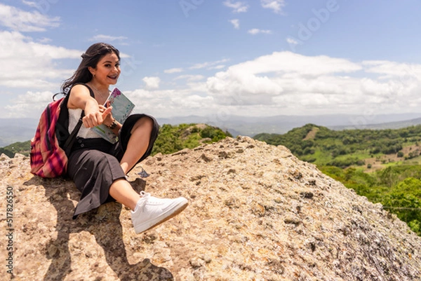 Fototapeta Female university student from Nicaragua smiling happy with thumb up sitting on a rock outdoors