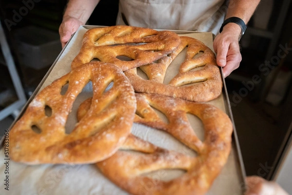 Fototapeta A man in a bakery takes traditional French Fougasse bread out of the oven. Front view.