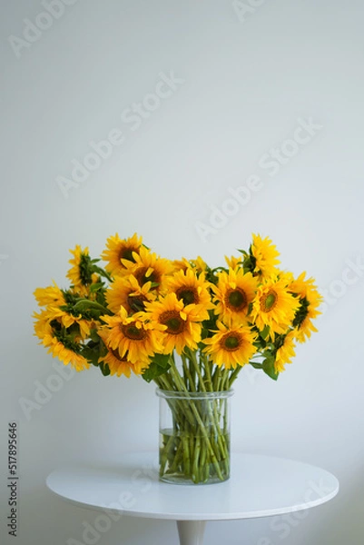 Fototapeta A large beautiful bouquet of traditional Ukrainian sunflower flowers in a glass vase on a white table.