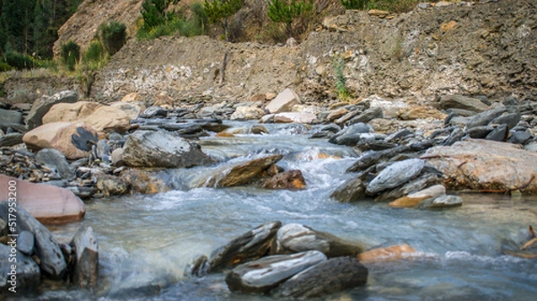 Fototapeta river with rocks in the foreground and bushes in the background, urcospampa, cusco, peru