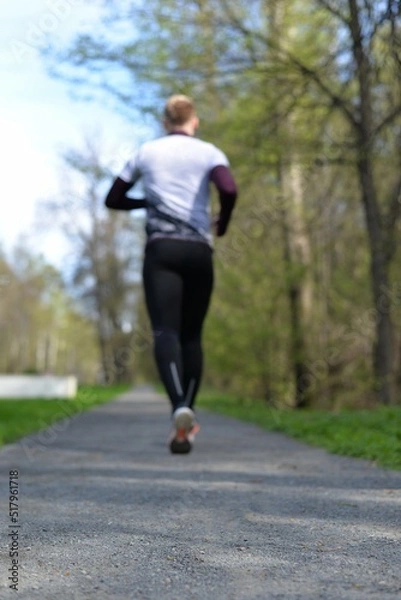 Fototapeta Silhouette of a person running along the path. A man is jogging in the park. Sportswear. Healthy lifestyle.
