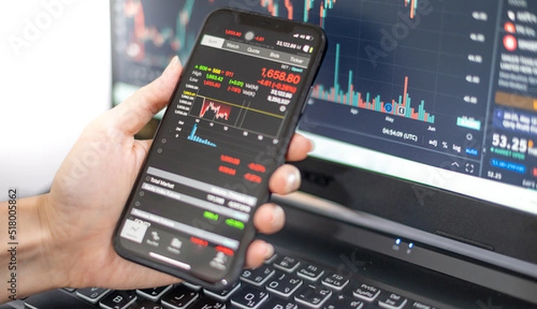 Fototapeta Female trader investor broker analyst holding a smartphone in hand analyzing stock market trading charts indexes data checking price using mobile