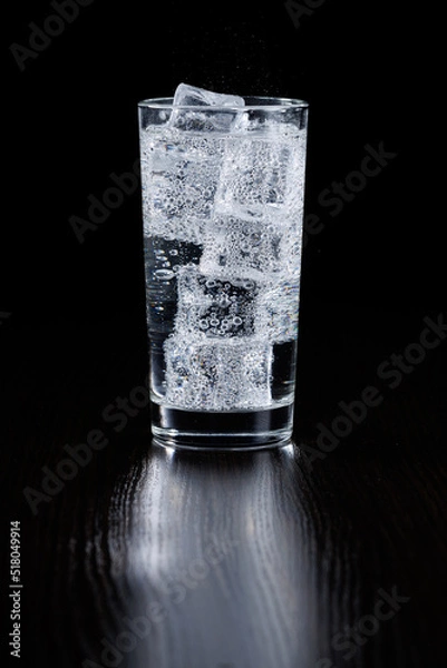 Obraz Sparkling mineral water with ice in a transparent glass on a black background.