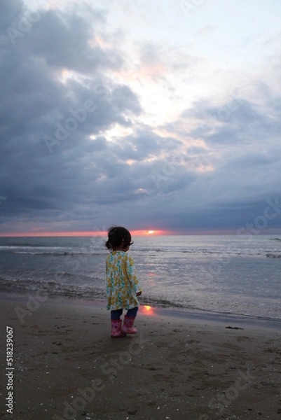 Obraz 水平線に沈む夕日を見つめる小さな女の子の後ろ姿