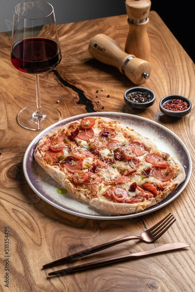 Obraz Roman pizza with salami, cherry tomatoes and parmesan with a glass of wine on a wooden table