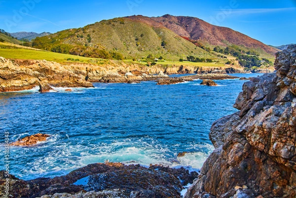 Fototapeta Waves crashing onto beach with tide pools and mountains in background