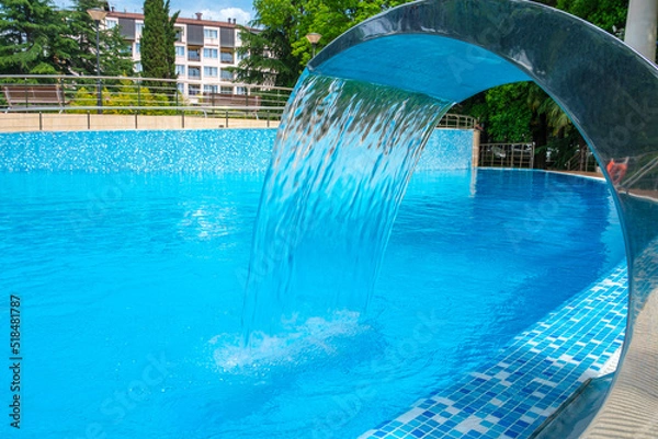 Obraz Pool side. Empty outdoors swimming pool and waterfall jet on summer sunny day. Seaside vacation and hotel resort concept. Reflection in blue clean sea water pool