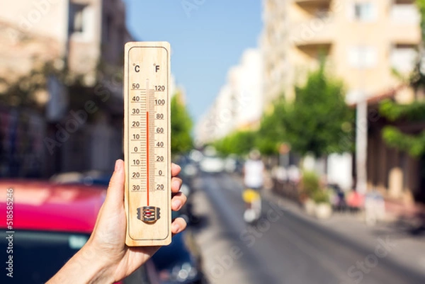 Fototapeta Hot weather. Thermometer in front of an urban scene during heatwave.