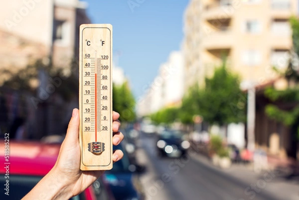 Fototapeta Hot weather. Thermometer in front of an urban scene during heatwave.