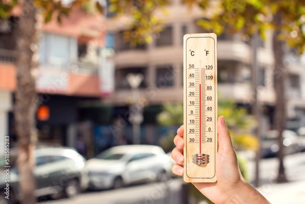 Fototapeta Hot weather. Thermometer in front of an urban scene during heatwave.