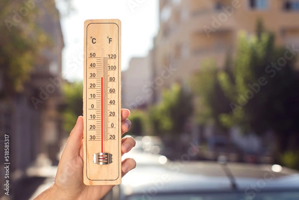 Fototapeta Hot weather. Thermometer in front of an urban scene during heatwave.