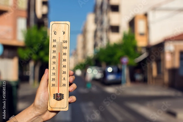 Fototapeta Hot weather. Thermometer in front of an urban scene during heatwave.