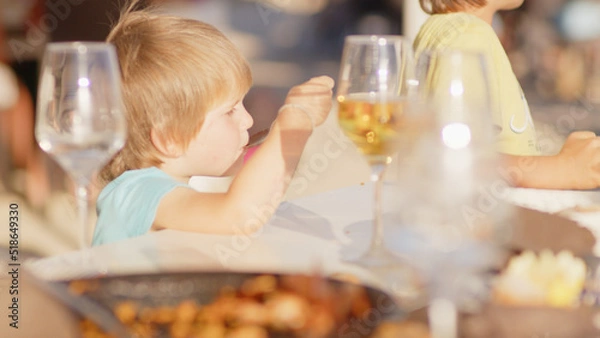 Fototapeta Family and friends gathered for lunch enjoying a delicious paella in a bar on the beach - happy little kids playing around the table after eating, eating dessert and ice cream